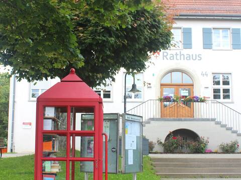 Im Vordergrund ist eine rote Bücherzelle zu sehen, dahinter das Horgenzeller Rathaus und ein grüner Baum