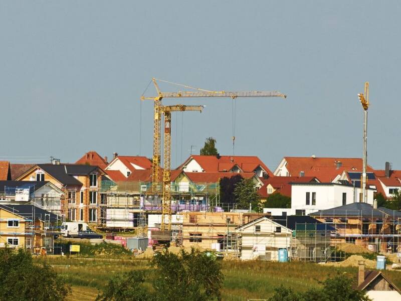 Blick von weitem aus der grünen Natur in ein Wohngebiet mit vielen Baukränen