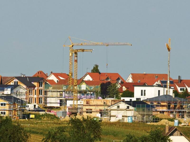 Blick von weitem aus der grünen Natur in ein Wohngebiet mit vielen Baukränen