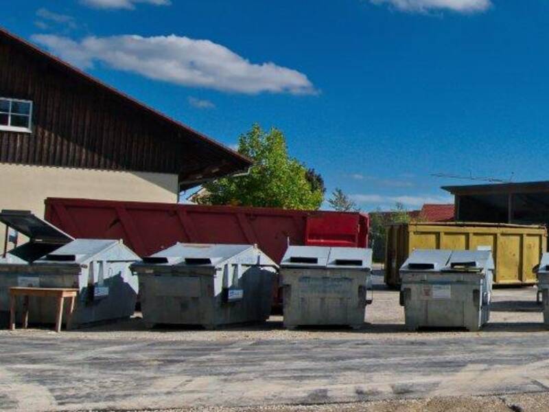 Ein asphaltiertes Gelände mit großen Containern ist zu sehen. Im Hintergrund große Wirtschaftsgebäude mit großen Toren. Es ist der Wertstoffhof der Gemeinde Horgenzell mit Abfallcontainern