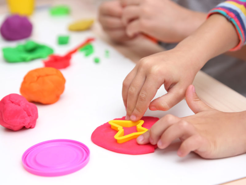 Bunte Knete wird auf einem Tisch von Kindern bearbeitet und mit einem Sternausstecher werden Formen ausgestochen