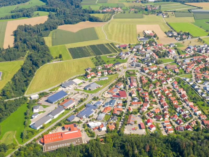 Luftaufnahme, die den gesamten Kernort Horgenzell erfasst, im Umland sind grüne Landschaften zu sehen.