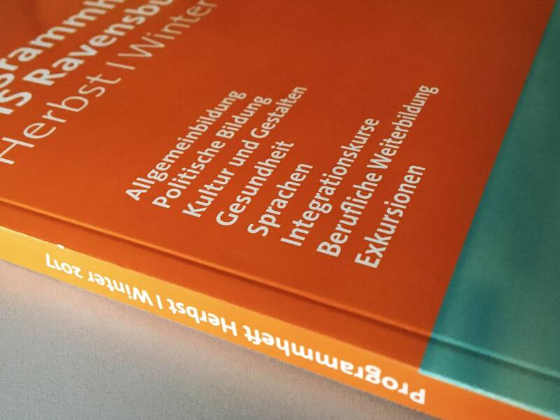 Programmheft der Volkshochschule als Buch gebunden in den Farben orange und türkis mit weißer Aufschrift.