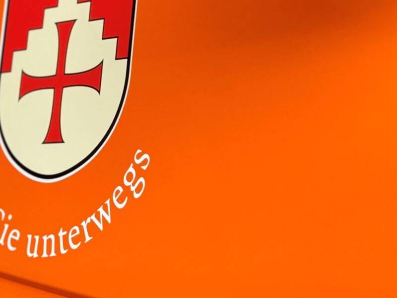 Eine Beifahrertür in Detailaufnahme, der Lack des Fahrzeugs ist orange. Darauf ist das Wappen der Gemeinde Horgenzell gedruckt, über dem Wappen steht "Horgenzell" darunter steht der Slogen "für Sie unterwegs" abgedruckt. Es ist eine Detailaufnahme des Bauhofunimogs.