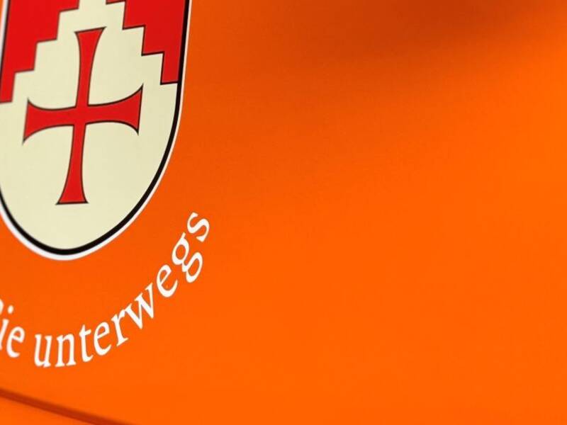 Eine Beifahrertür in Detailaufnahme, der Lack des Fahrzeugs ist orange. Darauf ist das Wappen der Gemeinde Horgenzell gedruckt, über dem Wappen steht "Horgenzell" darunter steht der Slogen "für Sie unterwegs" abgedruckt. Es ist eine Detailaufnahme des Bauhofunimogs.