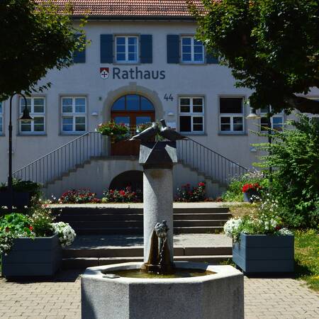 Blick auf das Rathaus Horgenzell. Im Vordergrund ein Brunnen, dahinter der Treppenaufgang zum Rathaus und das mit Fensterläden versehene Gebäude